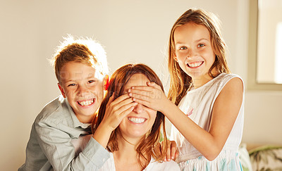 Buy stock photo Shot of two adorable children bonding with their mother at home and covering her eyes to surprise her