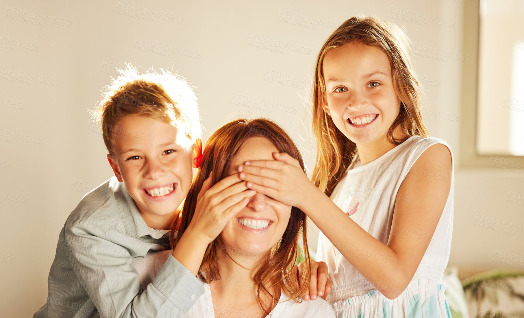 Buy stock photo Shot of two adorable children bonding with their mother at home and covering her eyes to surprise her