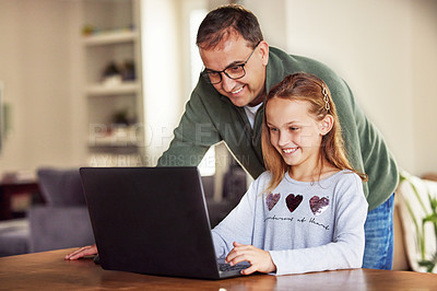 Buy stock photo Shot of an adorable little girl sitting and using a laptop at home while her father helps her