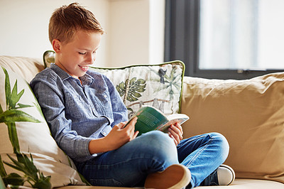 Buy stock photo Shot of an adorable little boy sitting alone on the sofa at home and reading a book