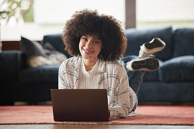 Buy stock photo Shot of a young woman laying on the floor and using her laptop at home