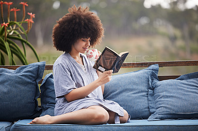 Buy stock photo Shot of an attractive young woman relaxing with a book outside on the patio