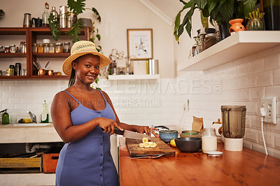 Buy stock photo Portrait of a young beautiful woman wearing a sunhat while slicing fruit in the kitchen at home