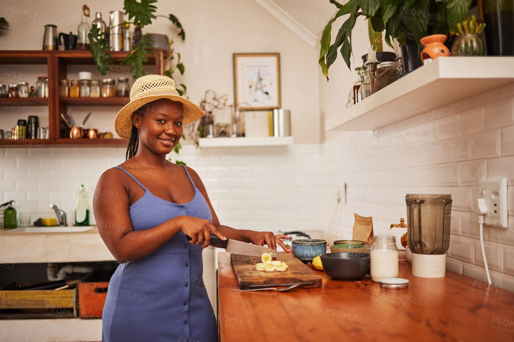 Buy stock photo Portrait of a young beautiful woman wearing a sunhat while slicing fruit in the kitchen at home