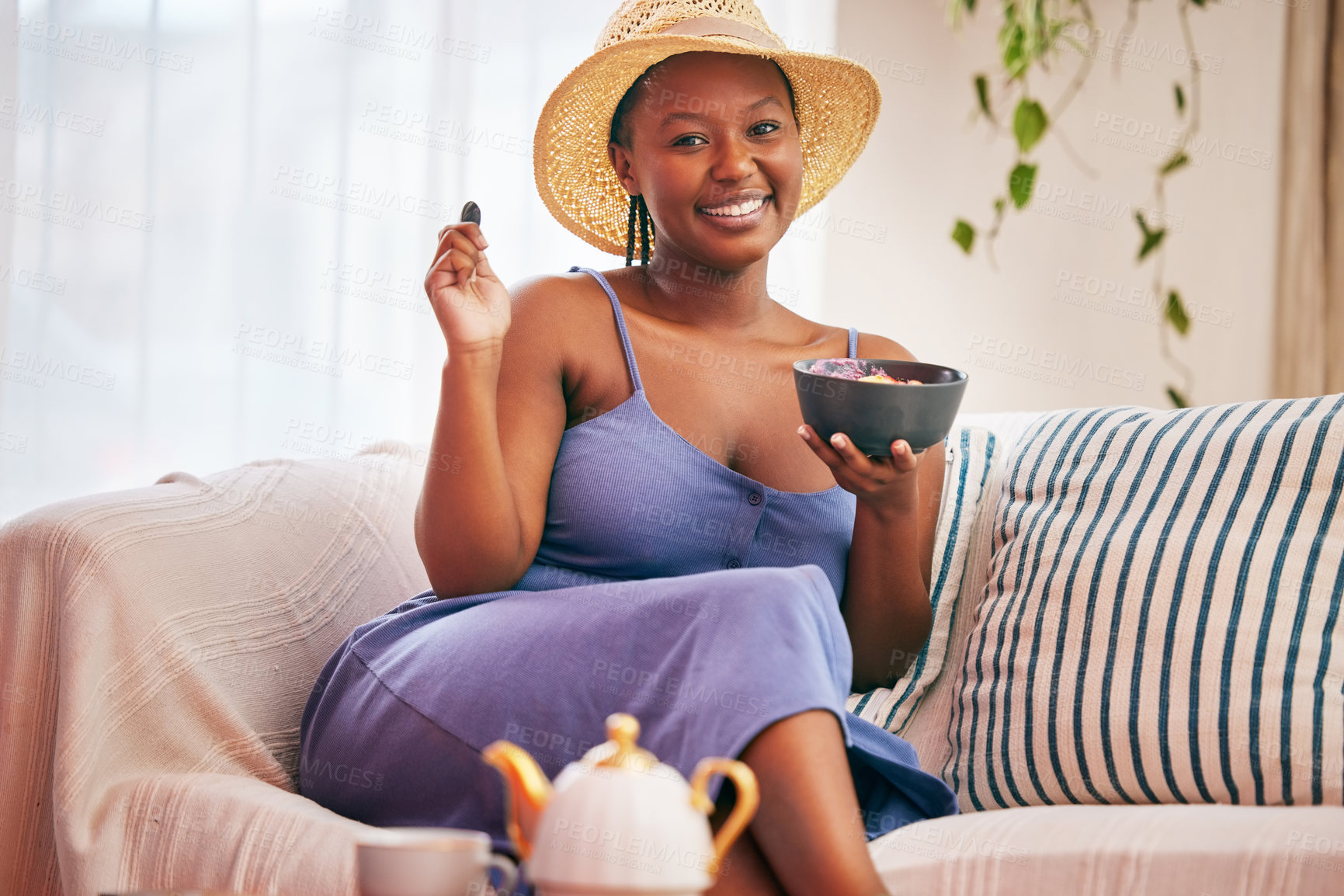 Buy stock photo Portrait of a young beautiful woman wearing a sunhat and having breakfast on the sofa at home