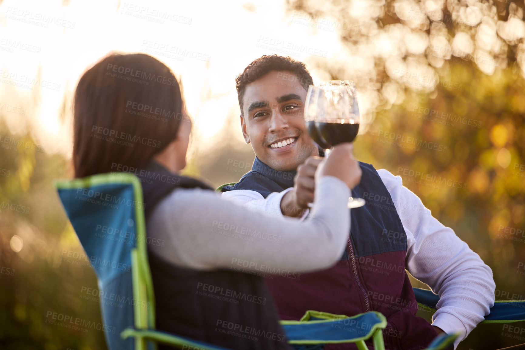 Buy stock photo Camping, wine and happy couple in park for toast of love, holiday vacation and valentines day picnic. Cheers, man and woman with care, smile and chairs on date for anniversary in nature or forest