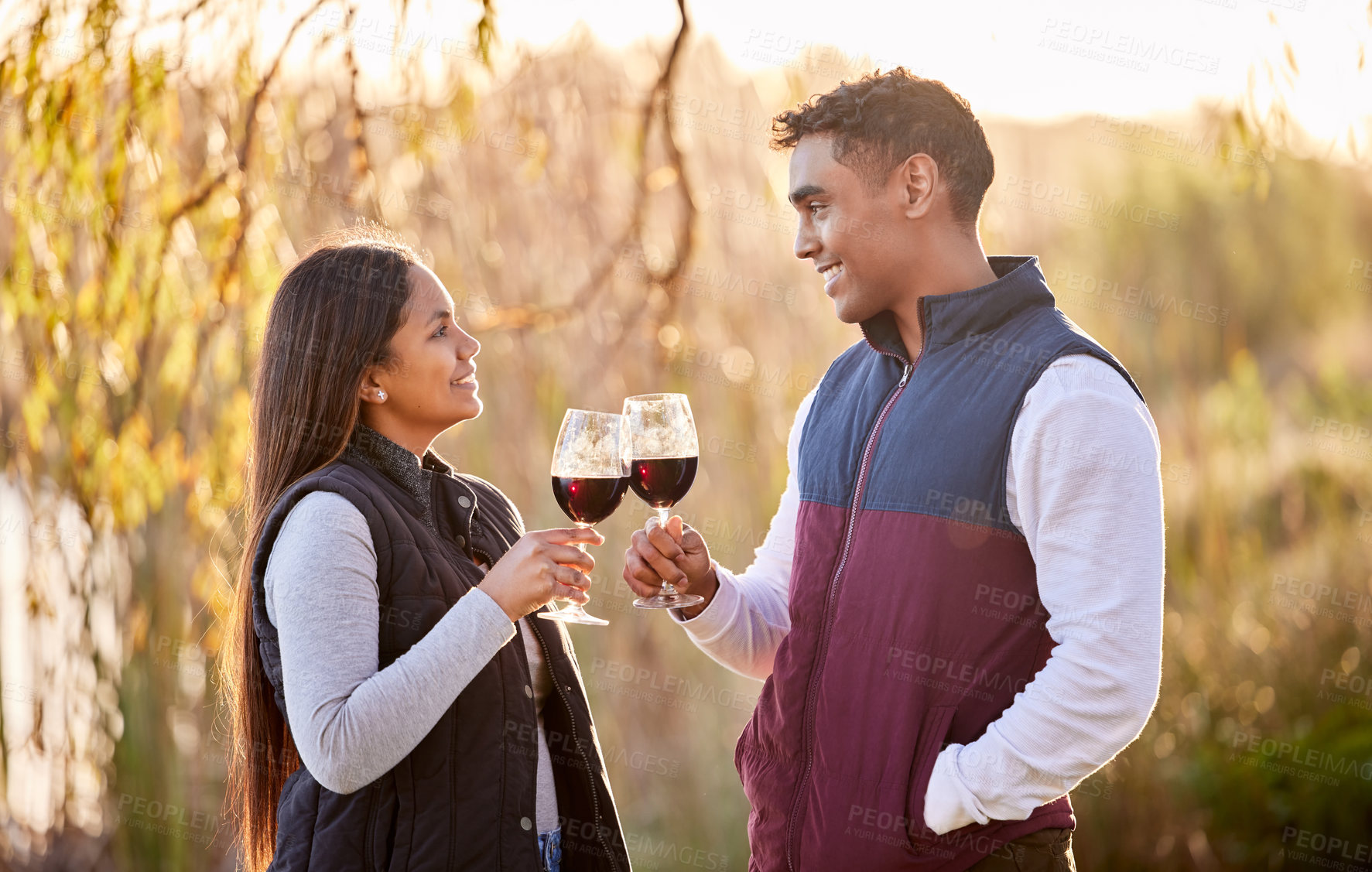 Buy stock photo Shot of a young couple having a glass outside while camping outside