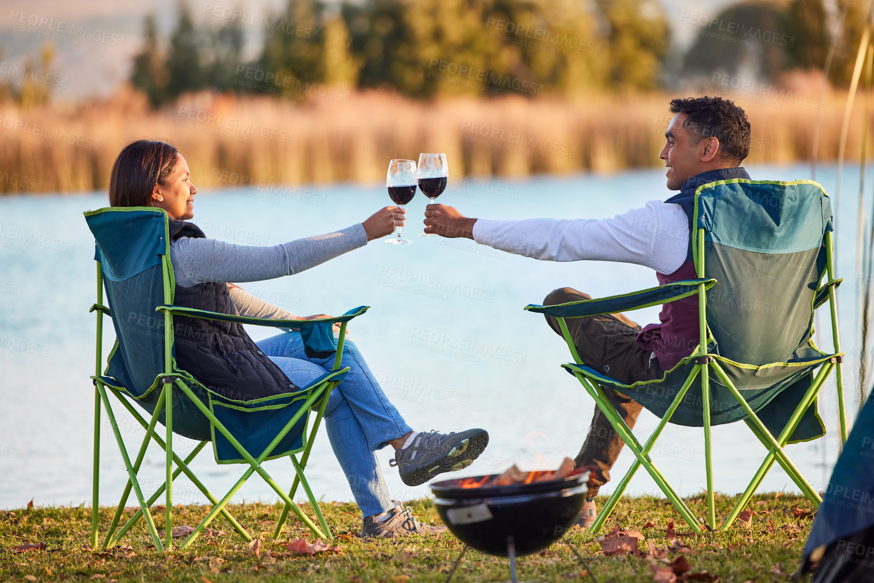 Buy stock photo Shot of a young couple having a glass outside while camping outside