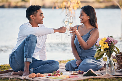 Buy stock photo Shot of a young couple making a toast while on a picnic at a lakeside