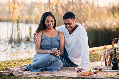 Buy stock photo Couple, picnic and phone for social media in outdoors, nature and relax on grass for bonding. People, lake and app for funny joke or online humor on vacation, travel and browse tech on park date
