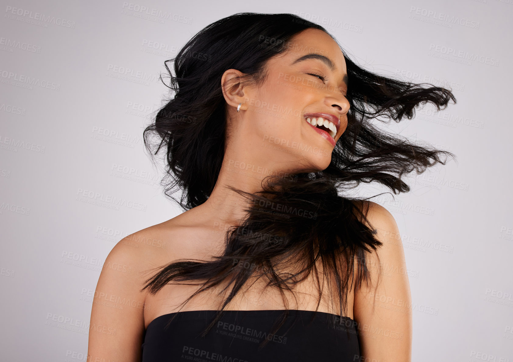 Buy stock photo Studio shot of a young woman shaking her hair while standing against a grey background