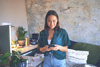 Buy stock photo Shot of an attractive young woman standing alone and using her cellphone to work from home