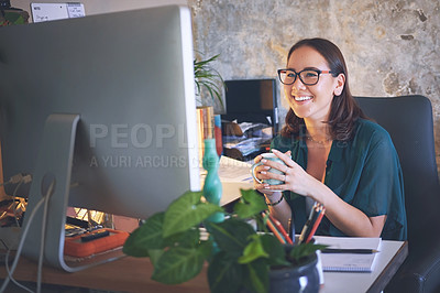 Buy stock photo Shot of a young woman sitting and enjoying a cup of coffee while using her computer to work from home