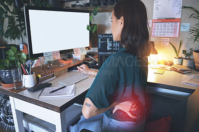 Buy stock photo Shot of a young woman sitting alone and suffering from back ache while using her computer to work from home