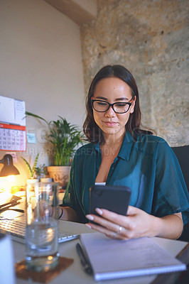 Buy stock photo Shot of an attractive young woman sitting alone and using her cellphone to work from home