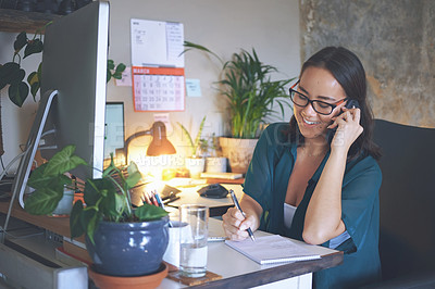 Buy stock photo Shot of an attractive young woman sitting alone and using her cellphone while writing notes in her home office