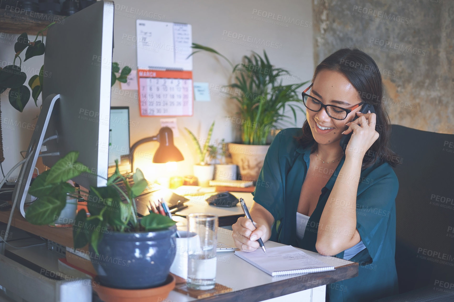 Buy stock photo Shot of an attractive young woman sitting alone and using her cellphone while writing notes in her home office