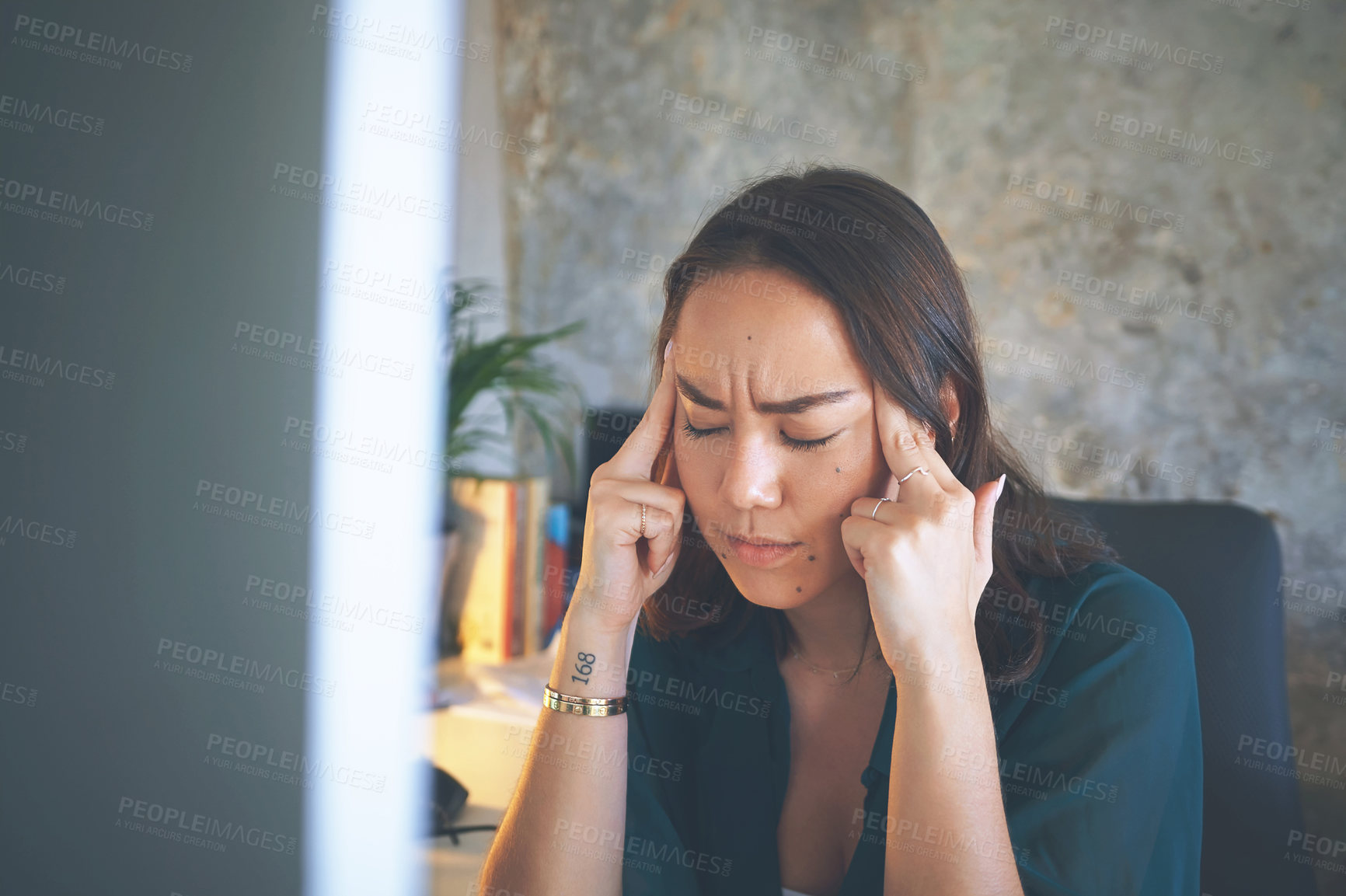 Buy stock photo Shot of an attractive young woman sitting and suffering from a headache while using her computer to work from home