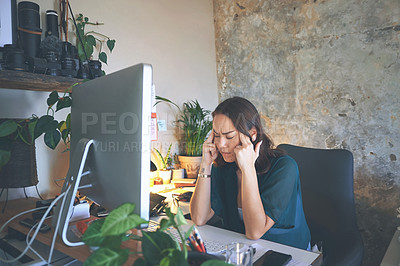 Buy stock photo Shot of an attractive young woman sitting and suffering from a headache while using her computer to work from home