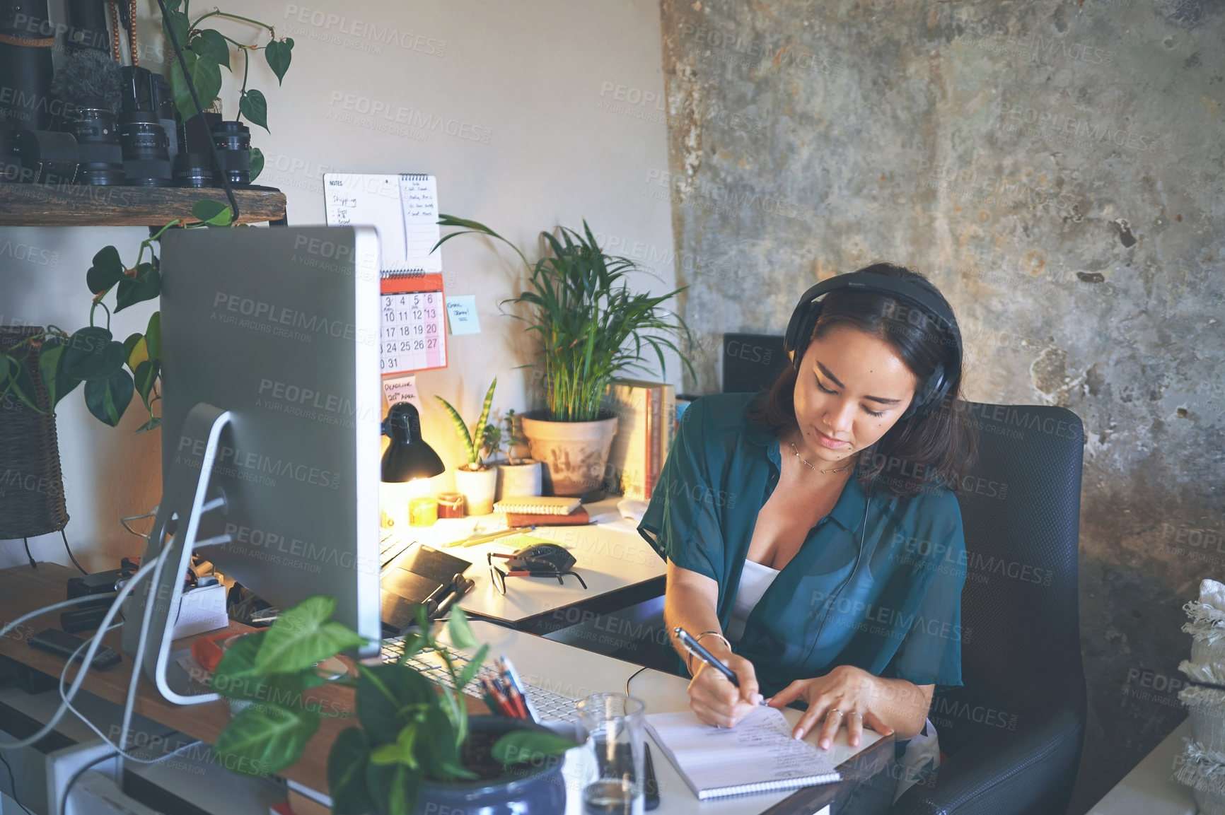 Buy stock photo Shot of an attractive young woman sitting alone and wearing a headset while writing notes in her home office