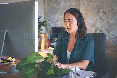 Buy stock photo Shot of an attractive young woman sitting alone and wearing a headset while using her computer to work from home