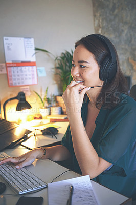 Buy stock photo Shot of an attractive young woman sitting alone and wearing a headset while working from home