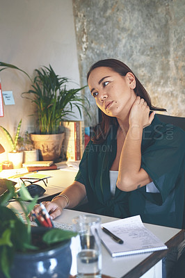 Buy stock photo Shot of an attractive young woman sitting alone and suffering from neck ache while working from home