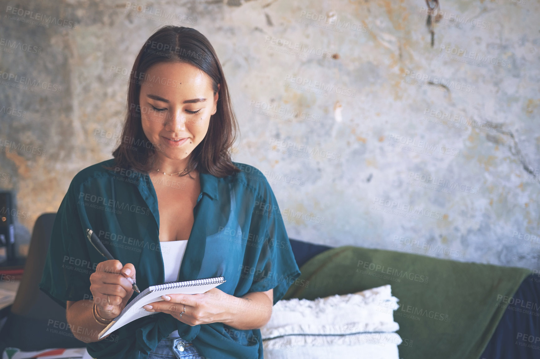 Buy stock photo Shot of an attractive young woman standing alone and writing notes while working from home