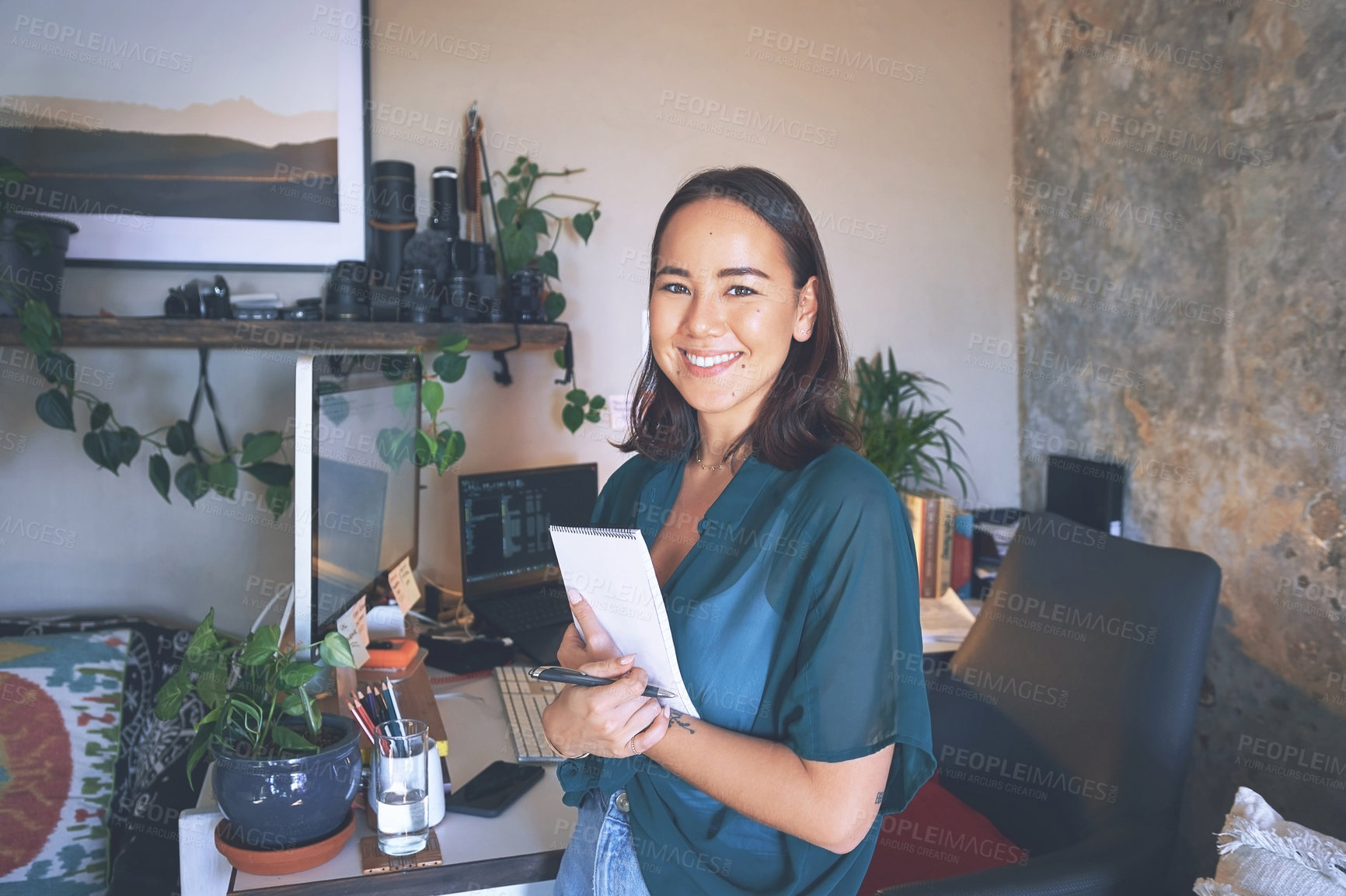 Buy stock photo Shot of an attractive young woman standing alone in her home office and holding her notepad