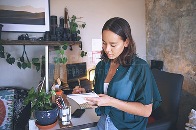 Buy stock photo Shot of an attractive young woman standing alone and looking contemplative while writing notes in her home office