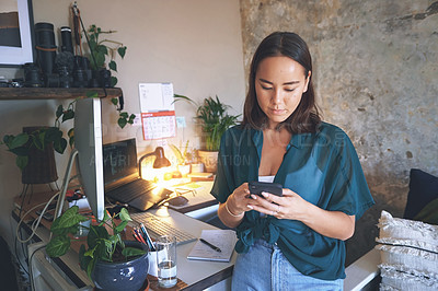 Buy stock photo Shot of an attractive young woman standing alone and using her cellphone to work from home