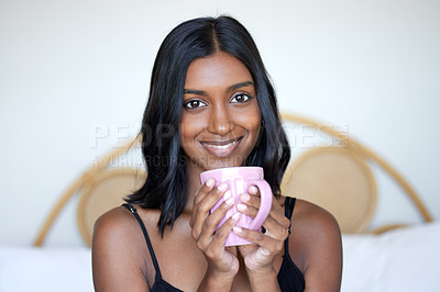 Buy stock photo Shot of a beautiful young woman holding a cup while sitting on her bed