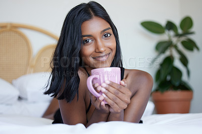 Buy stock photo Shot of a beautiful young woman holding a cup while lying on her bed