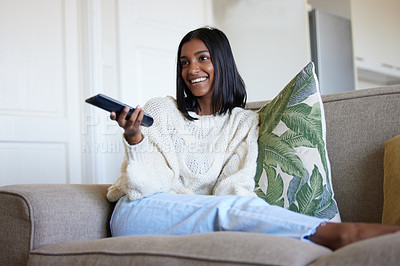 Buy stock photo Shot of a beautiful young woman holding a remote control while sitting on the couch at home