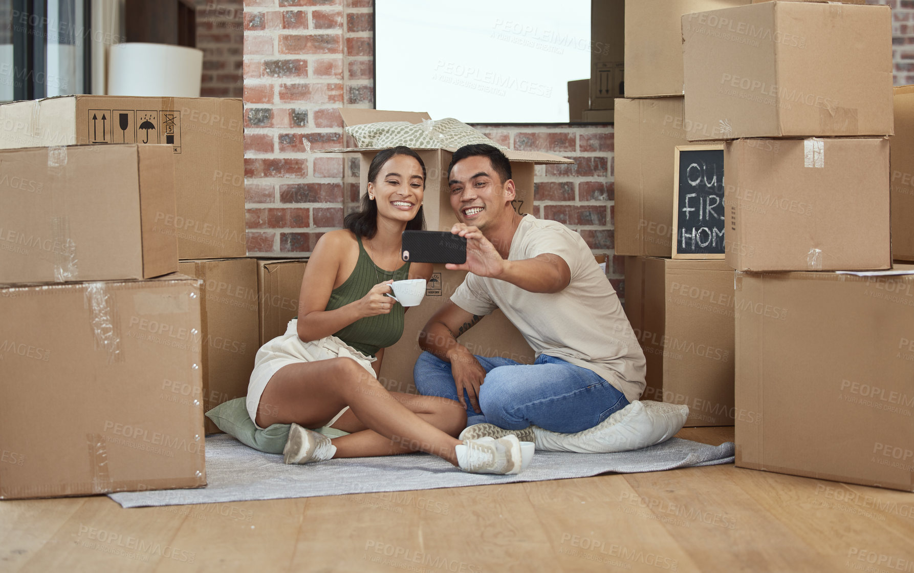 Buy stock photo Shot of a young couple taking a selfie while sitting in their new home