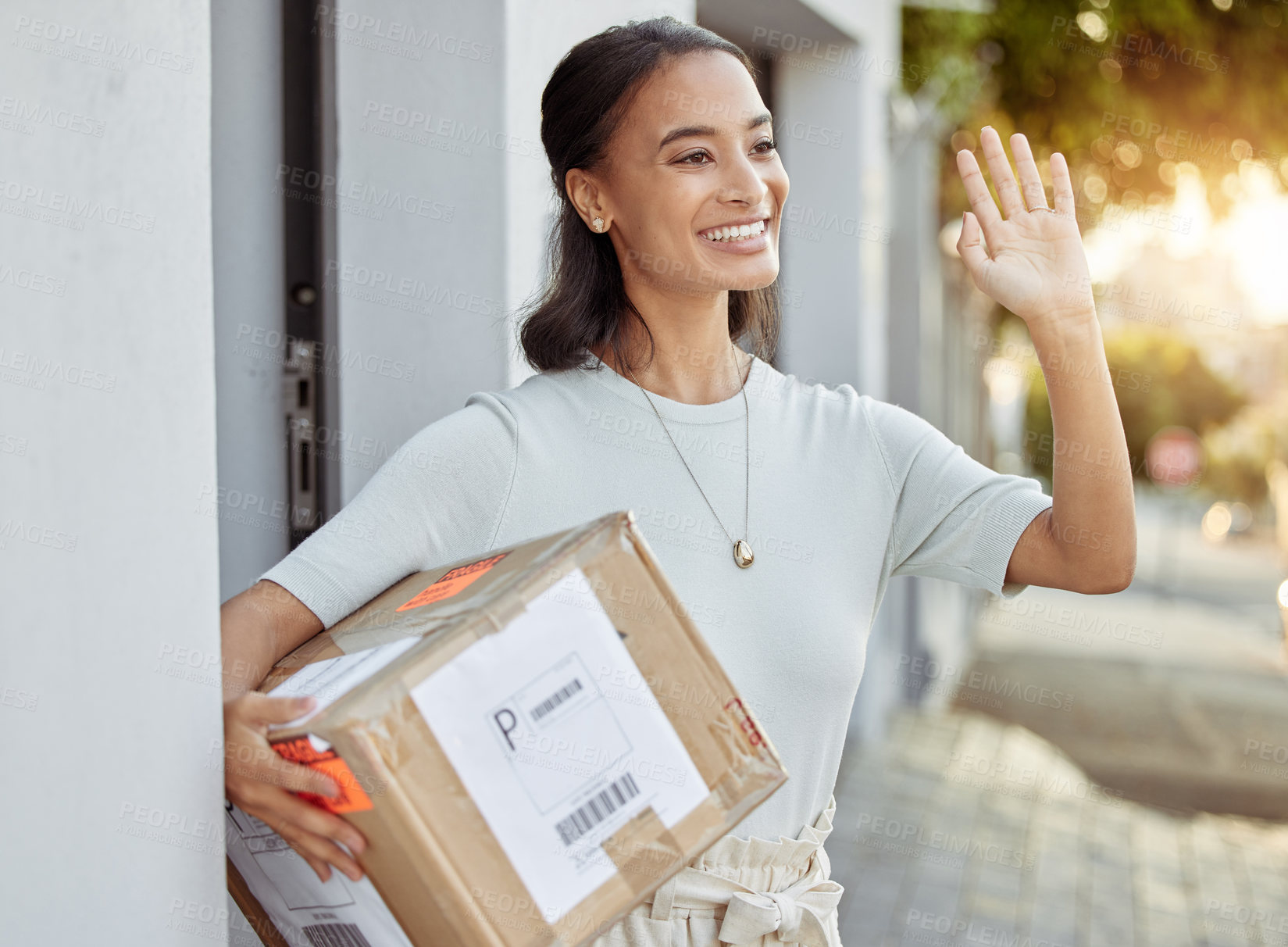 Buy stock photo Shot of a young woman waving to her delivery man after receiving a package