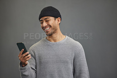 Buy stock photo Shot of a young man using his cellphone while standing against a grey background