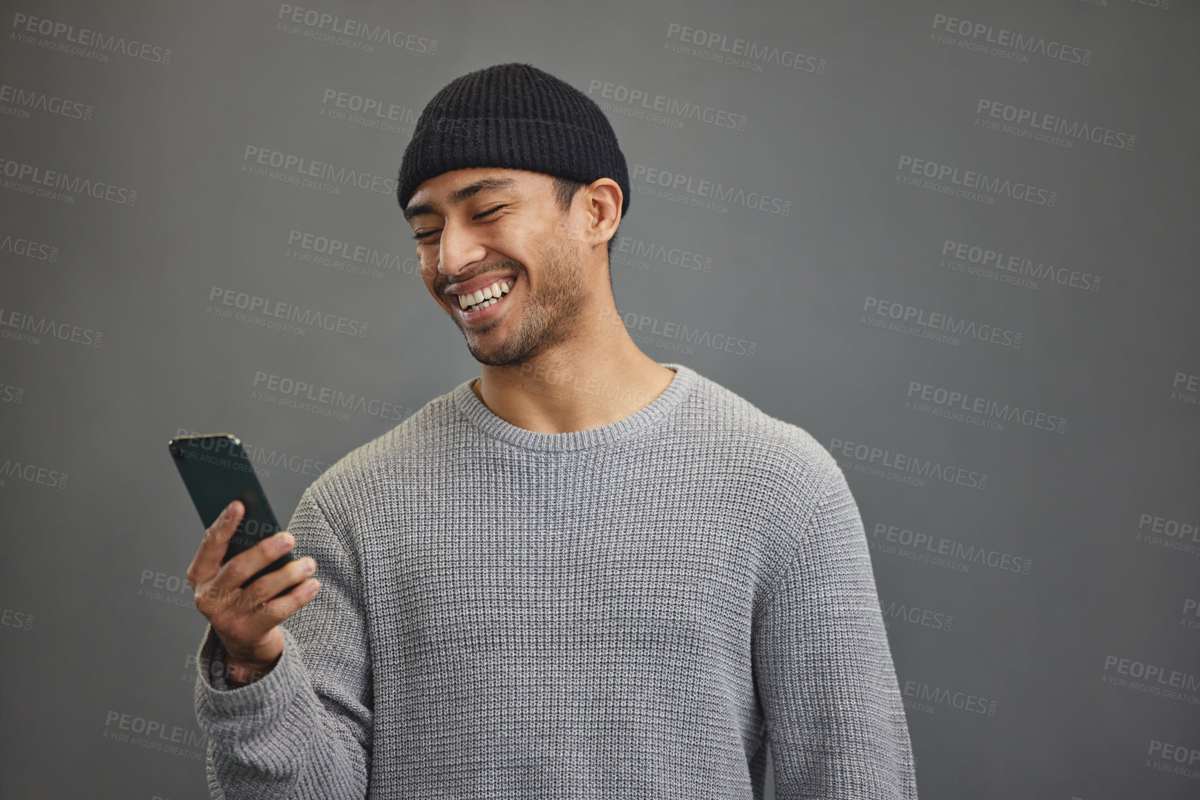 Buy stock photo Shot of a young man using his cellphone while standing against a grey background