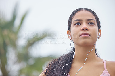 Buy stock photo Shot of a young woman listening to music through earphones while exercising