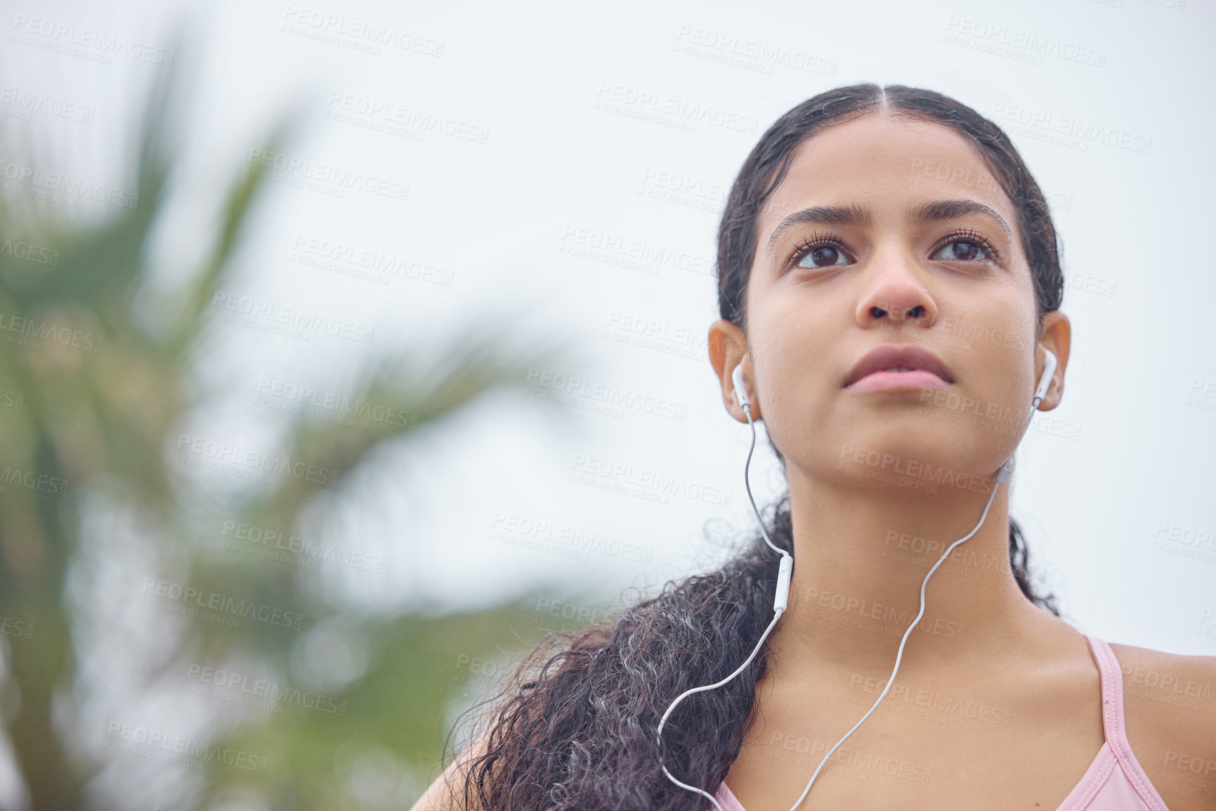 Buy stock photo Shot of a young woman listening to music through earphones while exercising