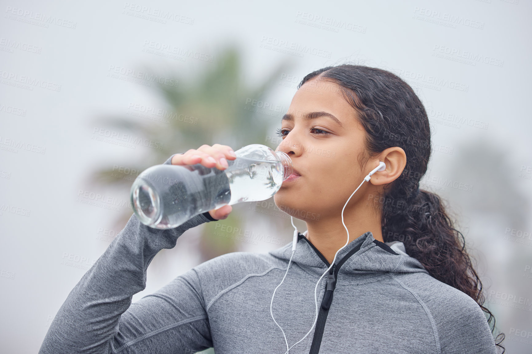 Buy stock photo Shot of a young woman drinking water while exercising in nature