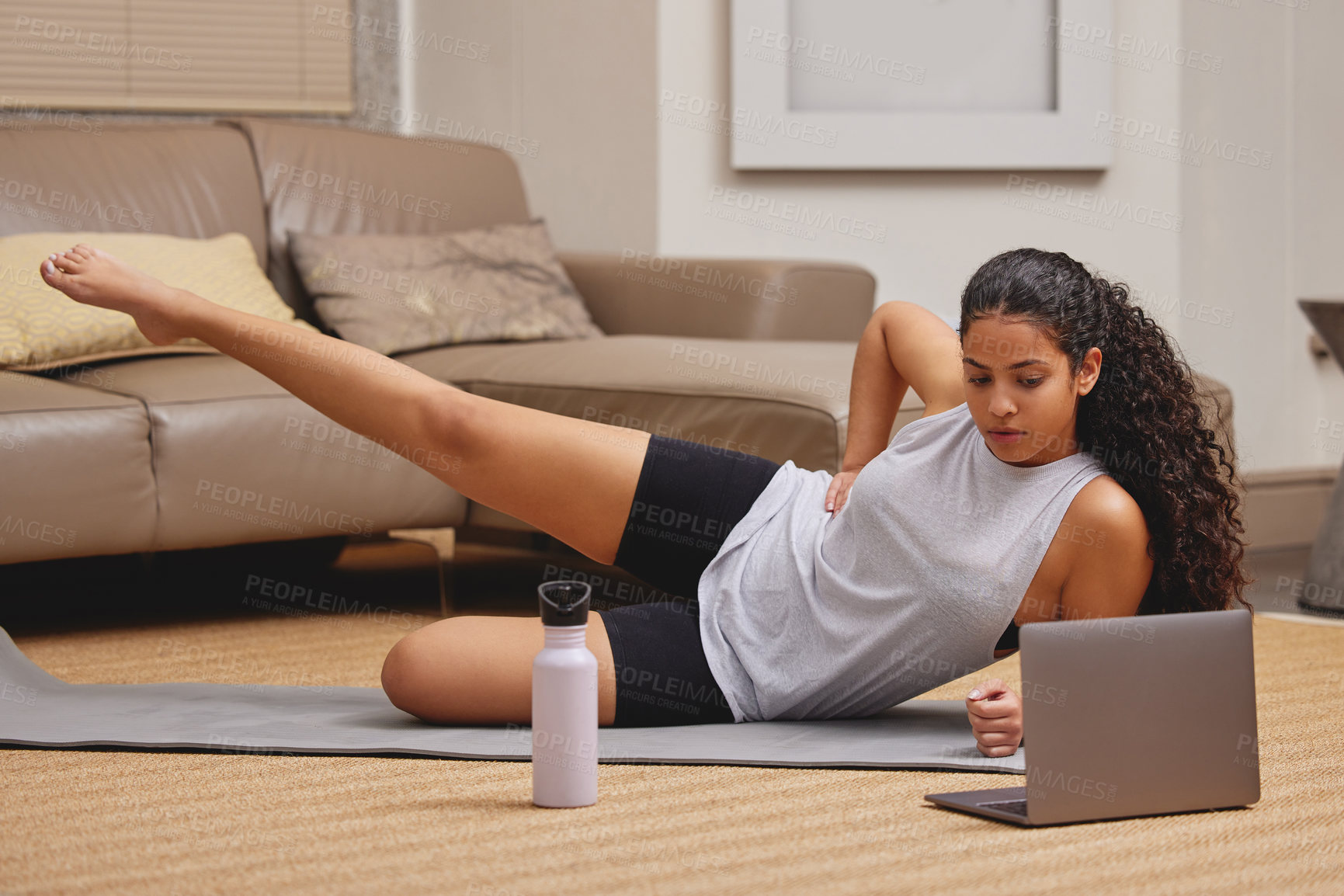 Buy stock photo Full length shot of a young woman using her laptop to follow an online fitness class in her living room