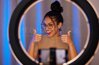 Buy stock photo Shot of a young woman showing a thumbs up while using a phone to film at home