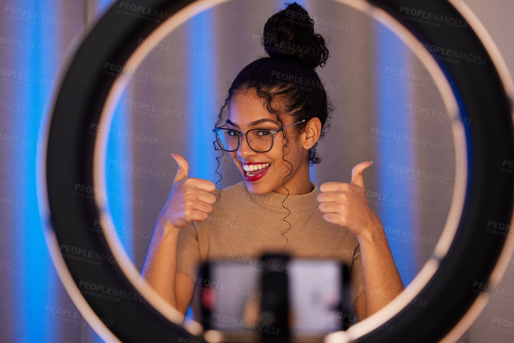 Buy stock photo Shot of a young woman showing a thumbs up while using a phone to film at home