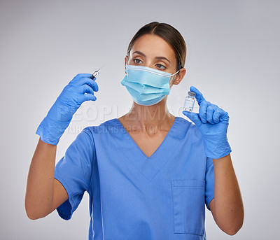 Buy stock photo Shot of a young female nurse holding a needle and vial of vaccination fluid against a studio background