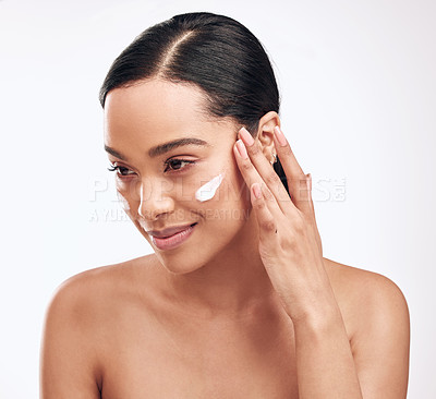Buy stock photo Studio shot of a beautiful young woman applying moisturiser to her face