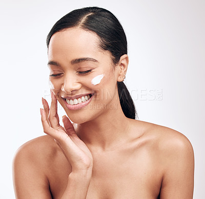 Buy stock photo Studio shot of a beautiful young woman applying moisturiser to her face