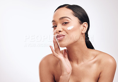 Buy stock photo Studio shot of a beautiful young woman applying moisturiser to her face