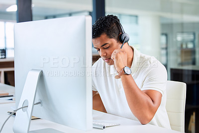Buy stock photo Shot of a handsome young businessman sitting alone in his office and wearing a headset while using his computer