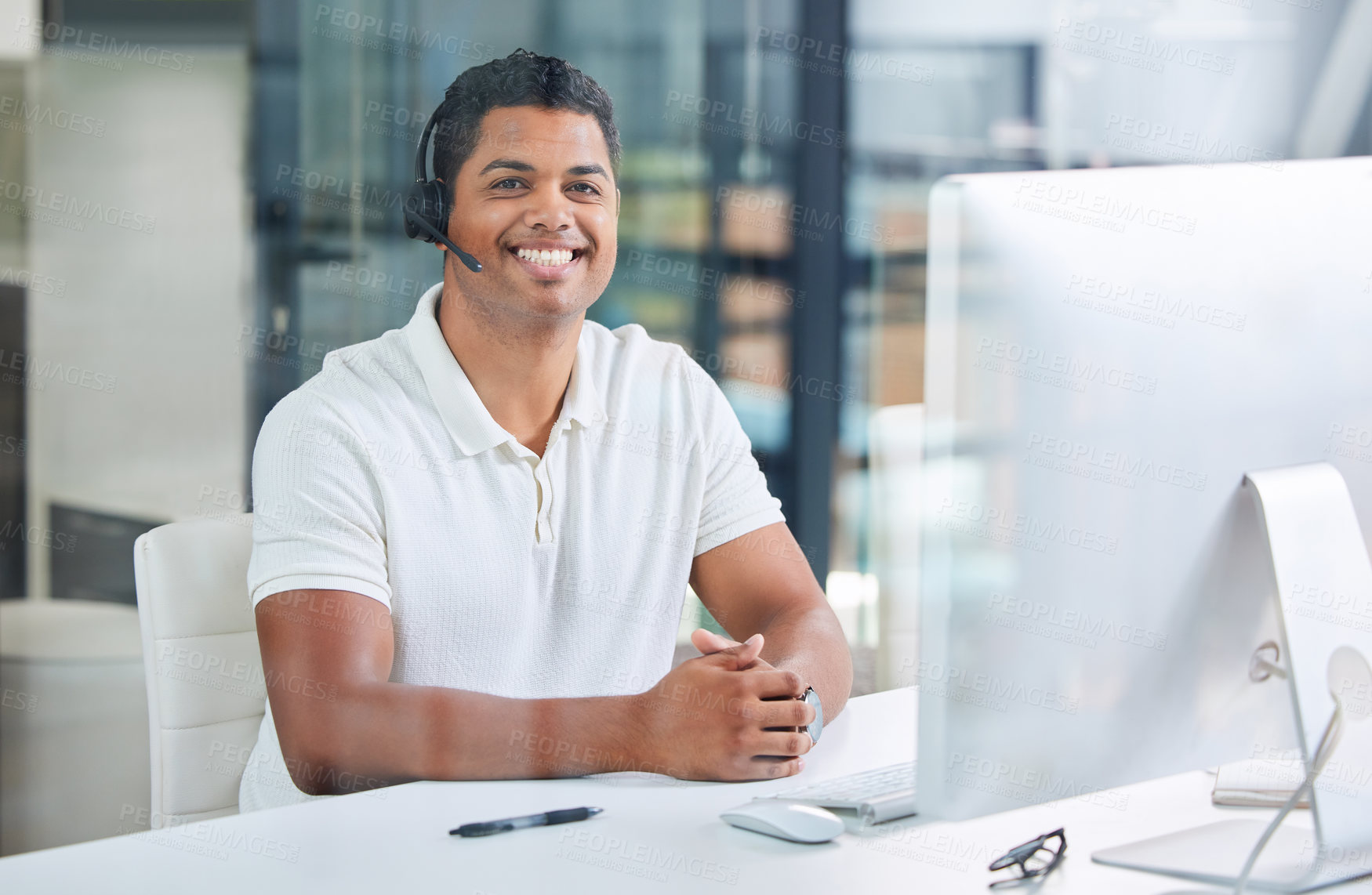 Buy stock photo Shot of a handsome young businessman sitting alone in his office and wearing a headset while using his computer